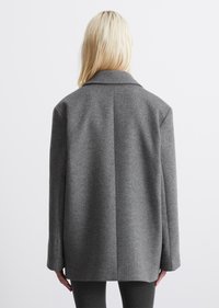 Cappotto grigio in lana con texture, colletto a revers, maniche lunghe e taglio dritto. La vista posteriore mostra una cucitura pulita al centro.