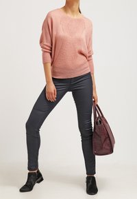 Maglione rosa lavorato a maglia con un motivo a diamante, abbinato a pantaloni scuri aderenti grigi e stivaletti neri alla caviglia. Include una borsa con texture in coccodrillo bordeaux.