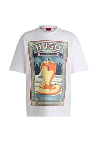 Balta medvilninė marškinėlių su dideliu spalvingu kobros grafiku, apsuptu puošnių raštų ir užrašais "HUGO SINCE 1993" ir "WINNING BLEND."