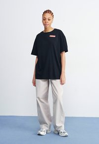 Black oversized t-shirt with short sleeves, featuring a small red label. Paired with light gray wide-leg pants and white sneakers.