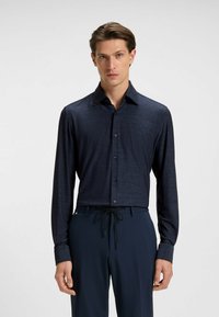 Camicia button-up a maniche lunghe navy con una texture sottile, colletto a punta e bottoni neri. Indossata con pantaloni scuri con cordoncino.