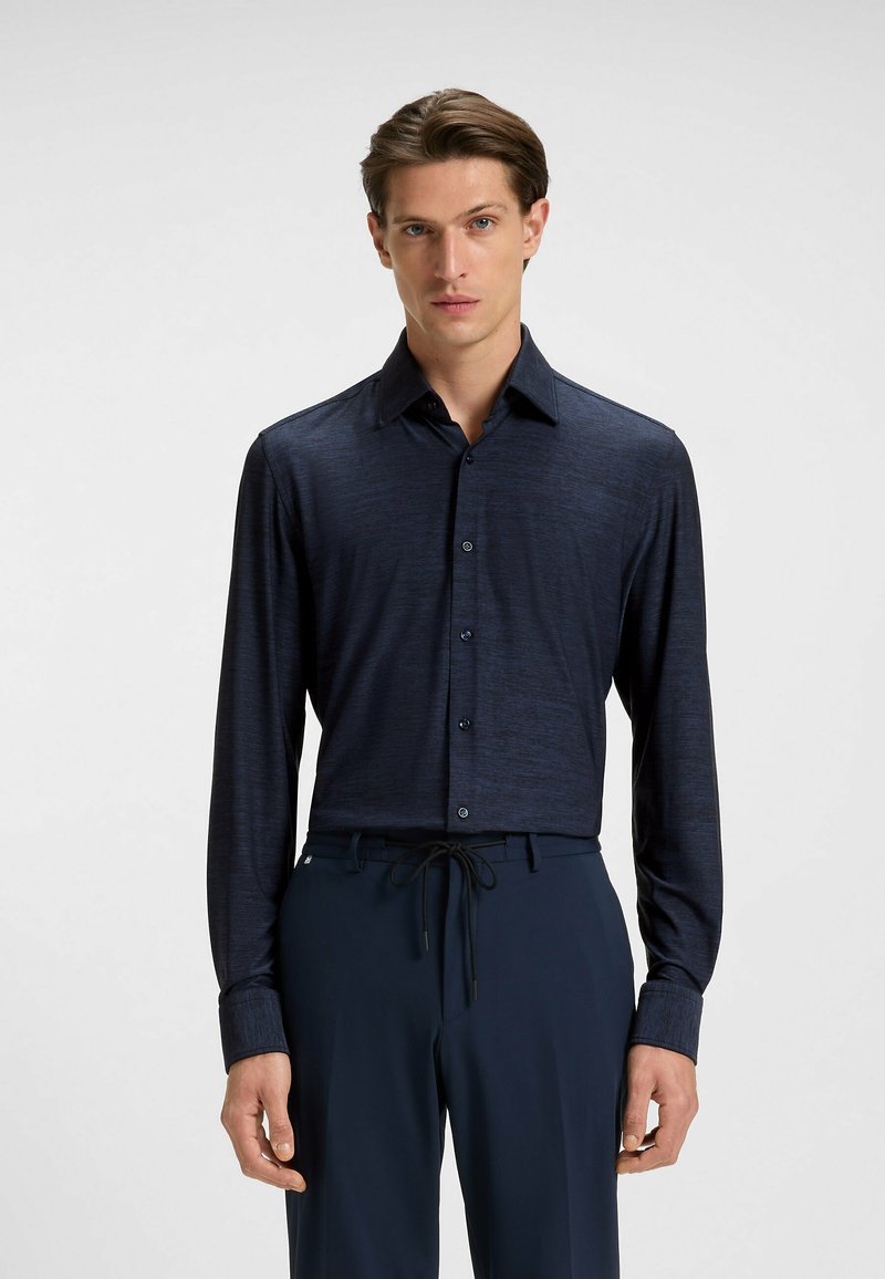 Camicia button-up a maniche lunghe navy con una texture sottile, colletto a punta e bottoni neri. Indossata con pantaloni scuri con cordoncino.