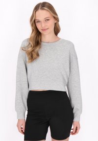 Grå kort sweatshirt med långa ärmar, tillverkad av mjukt tyg. I kombination med svarta högmidjade shorts. Modellen har vågigt hår.