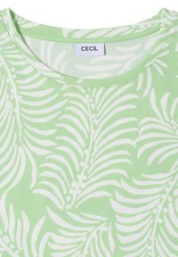 Chemise vert clair avec motif de feuilles tropicales blanches et encolure ronde avec une étiquette blanche avec texte noir.