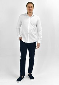 Witte langemouwen shirt met knopen, gecombineerd met donker marineblauwe slim-fit broek. Casual zwarte instap schoenen maken de outfit compleet.