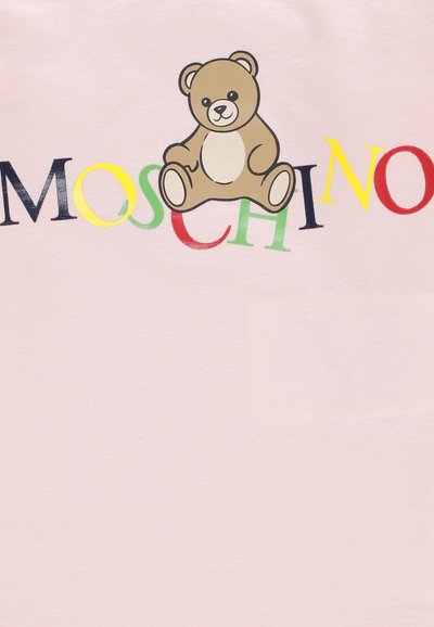 Orso di peluche marrone seduto sopra lettere MOSCHINO multicolori su uno sfondo di tessuto rosa chiaro.