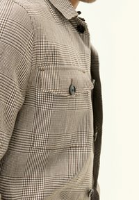 Brown and white plaid shirt with a collar, featuring a chest pocket and dark buttons, made of textured fabric.
