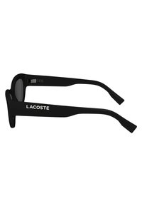 Black sunglasses with thick, rectangular frames. The temple has a white "LACOSTE" logo. Lenses are tinted gray, with smooth texture.