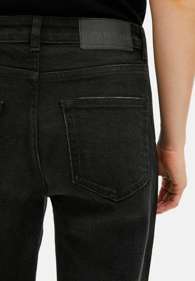 Jeans de mezclilla negros con una textura suave, diseño tradicional de cinco bolsillos y una etiqueta de marca visible en la cinturilla.