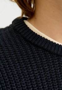 Dunkel gestrickter Pullover mit einem strukturierten, gerippten Kragen. Der Rundhalsausschnitt zeigt eine hellere innere Schicht darunter, die dem Design Kontrast verleiht.