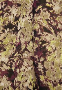 Tissu avec motif floral abstrait dans des tons vert olive, bordeaux, beige et noir, montrant la texture et les plis.