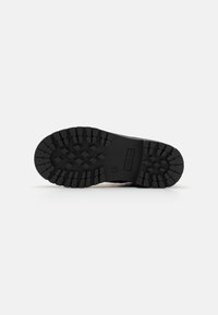 Suela de zapato de goma negra con un patrón de relieve profundo, que presenta acentos elevados y una textura duradera para proporcionar tracción y agarre.