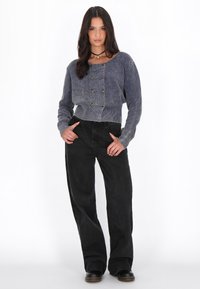 Maglione corto a maglia blu navy e azzurro chiaro con colletto rotondo e bottoni dorati, abbinato a pantaloni neri a vita alta con gamba larga e scarpe nere.