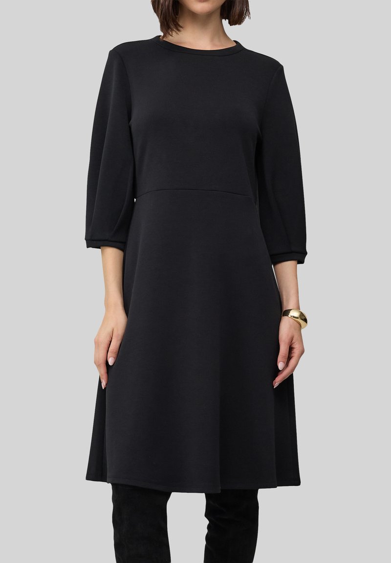 Czarna sukienka do kolan z miękkiego materiału, z rękawami do łokci, okrągłym dekoltem i rozkloszowanym dołem. Minimalistyczny design, bez wzorów.