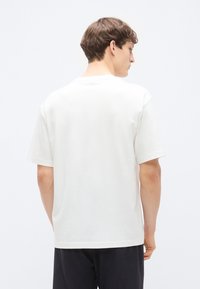 Λευκό βαμβακερό μπλουζάκι με κοντά μανίκια και λαιμόκοψη γύρω. Ομαλή υφή, χαλαρή εφαρμογή και μινιμαλιστικός σχεδιασμός. Εμφανίζεται η πίσω όψη.