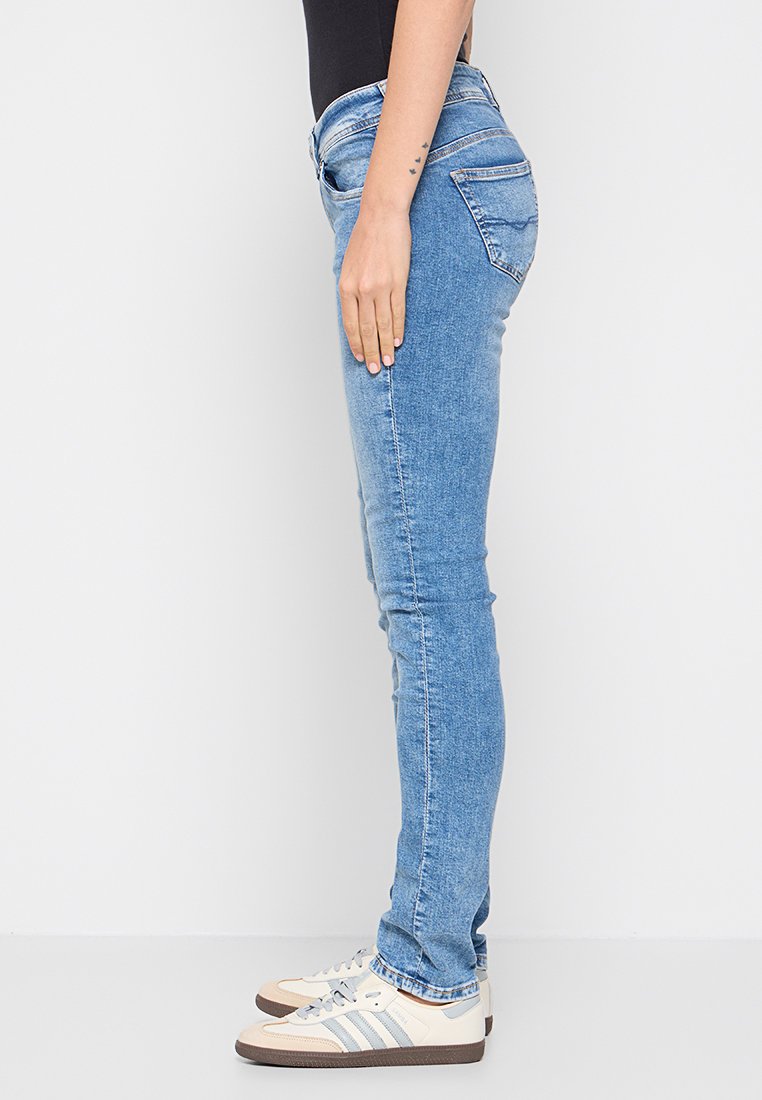 Helle blaue Skinny-Jeans mit glatter Textur, ausgestattet mit typischem Fünf-Taschen-Design und dezentem Ausbleichen. Kombiniert mit cremefarbenen Sneakers.