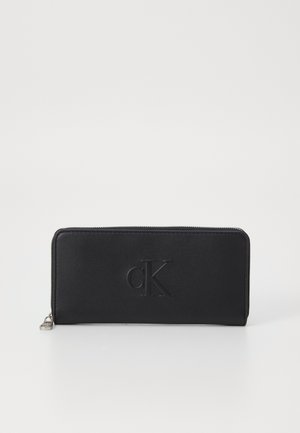 Portafoglio nero con zip in pelle liscia, caratterizzato da un logo "cK" in rilievo sul fronte e da una forma rettangolare elegante.