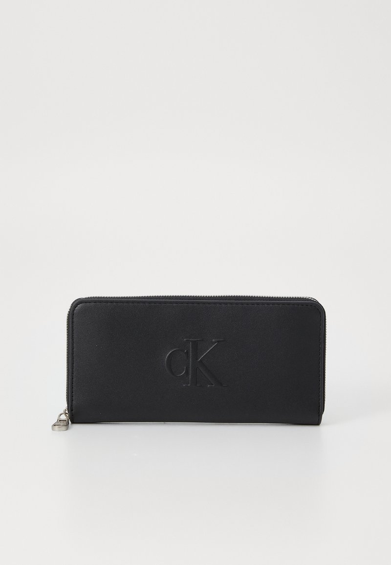 Portefeuille zippé noir en cuir lisse, avec un logo "cK" en relief à l'avant et une forme rectangulaire élégante.