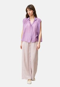 Lila Kurzarmbluse mit Knopfleiste, kombiniert mit weit geschnittenen gestreiften Hosen in Pastellorange und Blau.