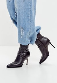 Zwarte, puntige enkellaarsjes met hoge hak, gecombineerd met lichtblauwe jeans versierd met hangende, doorzichtige kristalachtige versieringen.