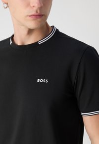 Sort T-shirt med ribbet krave, der har hvide og sorte striber. Branding "BOSS" i hvid placeret på venstre bryst. Glat tekstur.