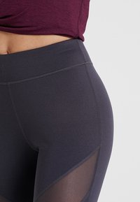 Czarne legginsy z wysokim stanem, z gładką fakturą, akcentami z siateczki oraz wzmocnionymi szwami dla większej trwałości.