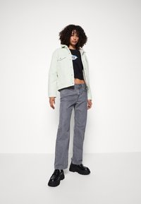 Giacca di jeans verde chiaro sopra una maglietta nera corta, abbinata a jeans dritti grigi e scarpe con plateau nere e spesse.