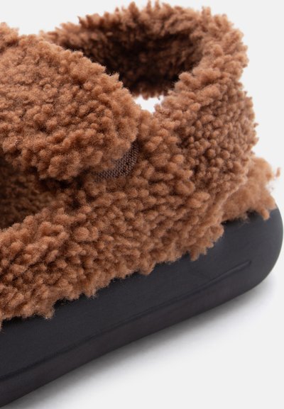 Καφέ αφράτη παντόφλα με μαύρη σόλα, που διαθέτει παχύ, άνετο επάνω μέρος από φλις και ανοιχτό πίσω μέρος.