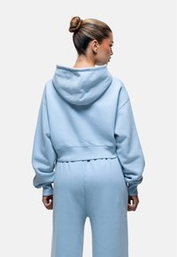 Felpa blu tagliata in tessuto morbido con un ampio cappuccio, maniche larghe e vestibilità rilassata, abbinata a pantaloni blu coordinati.