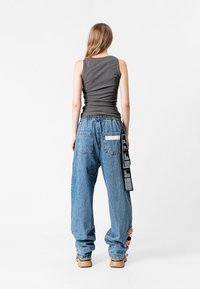 Camiseta sin mangas gris, pantalones vaqueros de denim azul sueltos con un detalle de tira negra, que incluyen un bolsillo y adornos de tela. Textura suave, ajuste casual.