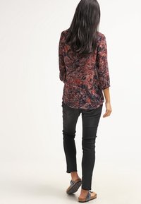Blusa de manga larga con estampado de cachemira en rojo y azul, combinada con jeans ajustados negros y sandalias color caramelo con un acento de lazo.