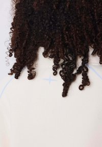 Riccioli scuri poggiano su un indumento di un beige chiaro con un sottile dettaglio di cucitura blu e un accento a forma di stella vicino allo scollo.