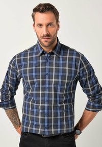 Camisa de cuadros en azul marino, negro y blanco; material de algodón, diseño abotonado, mangas enrolladas y botones visibles. Reloj negro en la muñeca.