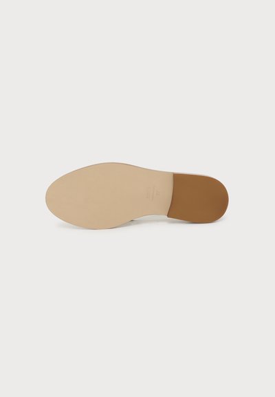 Semelle d’une chaussure habillée beige clair avec un talon marron contrastant, affichée à plat sur un fond clair uni.