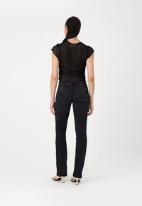Schwarzes Spitzenoberteil mit kurzen, rüschierten Ärmeln, kombiniert mit dunklen Jeans aus Denim, die über Gesäßtaschen und subtile Steppdetails verfügen.