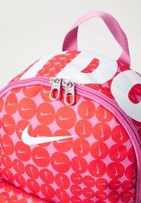 Κόκκινο και ροζ σακίδιο πλάτης με κυκλικό σχέδιο, που διαθέτει το λευκό λογότυπο της Nike και διπλούς μεταλλικούς φερμουάρ, μαζί με μια λαβή στην κορυφή για μεταφορά.