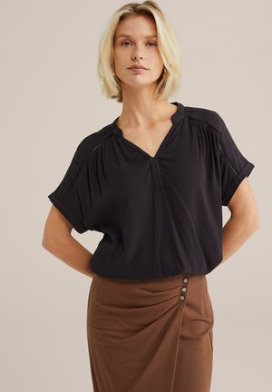 Zwarte blouse met korte mouwen, V-hals, geplooid ontwerp en subtiele stikdetails, gecombineerd met een bruine draperende rok met knoopaccenten.