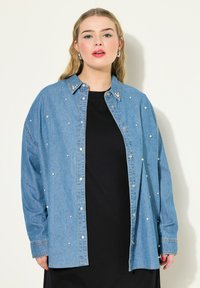 Camicia in denim con bottoni, caratterizzata da decorazioni in perle, maniche lunghe e colletto classico. Colore azzurro chiaro con una vestibilità comoda. Top nero sotto.