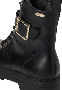 Bottine noire en cuir avec un col rembourré, accent en boucle en métal et semelle texturée. Design à lacets avec œillets en métal.