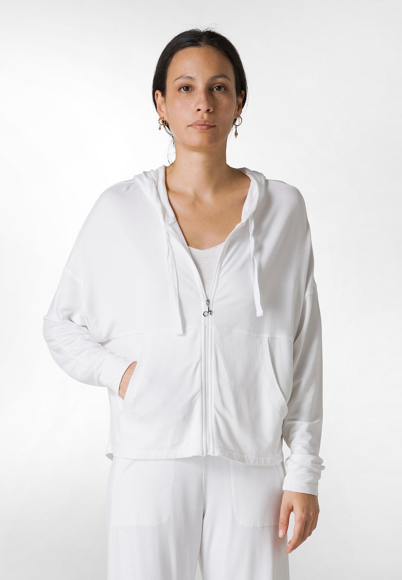 Hvid zip-up hoodie med en afslappet pasform, der har en hætte med snor, to frontlommer og lange ærmer. Blødt stof med en glat tekstur.