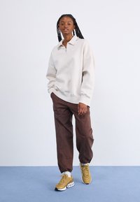 Light beige zip-up sweatshirt with a collar, paired with brown cargo pants and gold sneakers with white accents, set against a plain background.