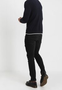 Pull marine avec une bordure blanche, associé à un jean skinny noir et des chaussures noires. Texture de tissu lisse et design ajusté.