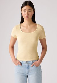 Ανοιχτό κίτρινο ριμπ μπλουζάκι με φαρδύ στρογγυλό ντεκολτέ και κοντά μανίκια. Φόρεμα εφαρμοστό, σε συνδυασμό με ανοιχτό μπλε τζιν ψηλόμεσο.