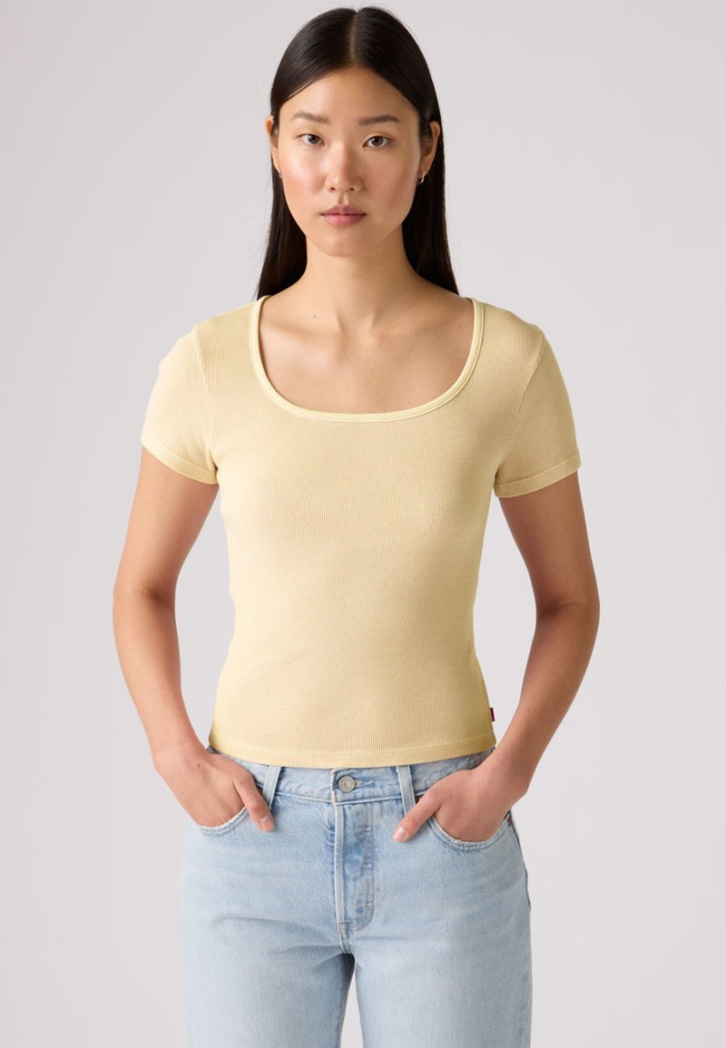 Ανοιχτό κίτρινο ριμπ μπλουζάκι με φαρδύ στρογγυλό ντεκολτέ και κοντά μανίκια. Φόρεμα εφαρμοστό, σε συνδυασμό με ανοιχτό μπλε τζιν ψηλόμεσο.