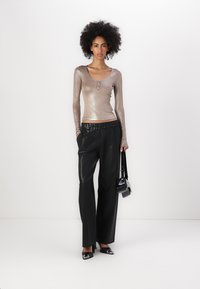 Langsleeve metallic top in lichtbrons met een ronde hals en knopdetail, gecombineerd met hoog-getailleerde zwarte faux leren wijde broek.