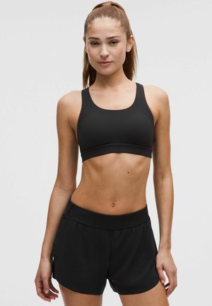 Sort atletisk sports-bh med brede stropper og glat tekstur, kombineret med matchende sorte shorts med elastisk taljebånd.