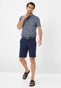 Kurzarmpolohemd mit Muster in Marineblau und geometrischem Design, kombiniert mit dunklen Shorts und schwarzen Badesandalen. Mit einem Gürtel.