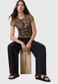 T-shirt aderente con stampa leopardata in marrone e nero, abbinata a pantaloni cargo neri larghi e sandali neri con borchie e una fibbia dorata.