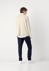 Beige langermet skjorte med teksturert finish, kombinert med marineblå bukser og hvite joggesko. Skjorten har en dropped shoulder-design.