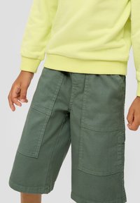 Groene cargoshorts met twee zijzakken, gemaakt van duurzaam katoen. Heeft een ontspannen pasvorm en een gestikte zoom. Gecombineerd met een gele sweatshirt.